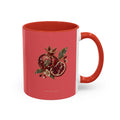 A ceramic mug with a coral red exterior, a white interior, and a handle matching the exterior. The front of the mug features a detailed illustration of a pomegranate, both whole and sliced open to reveal seeds, accompanied by green leaves and small flowers.